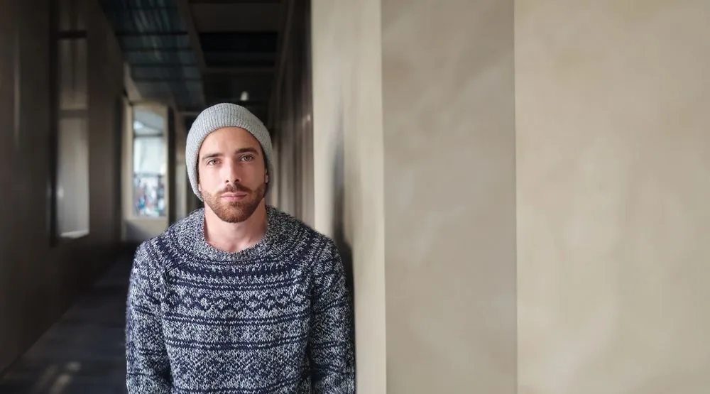 Rickard Lindbom in a grey beanie and a knitted sweater, standing in a hallway.